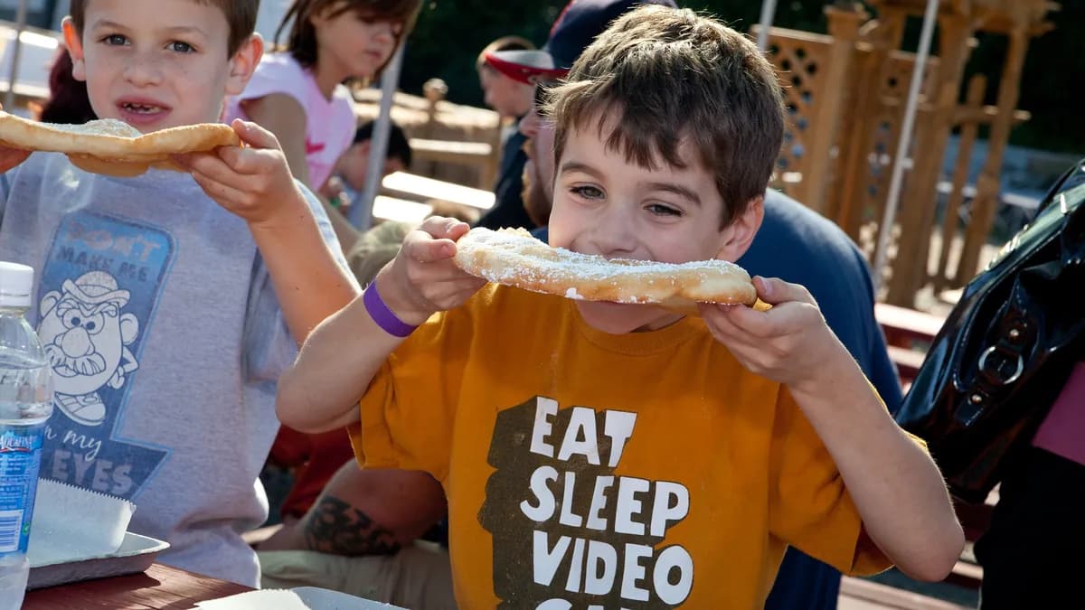 Two boys eating powdered-sugar fried dough at a picnic table