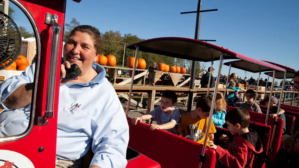 Operator driving a red barrel train full of kids with pumpkins behind